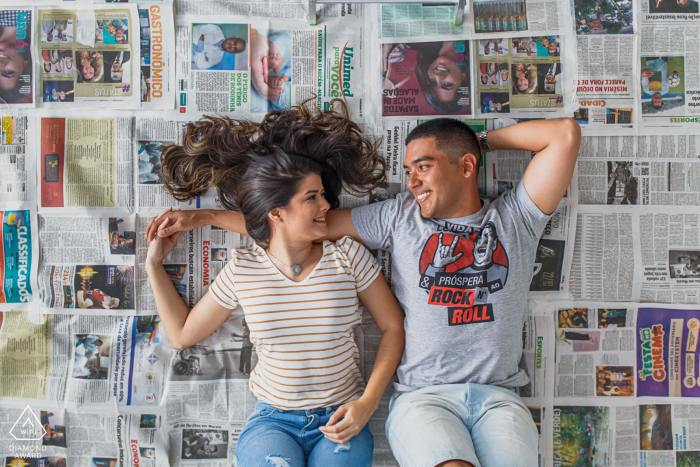 Porträtsitzung „True Love Engagement“ in Maceió mit einem Paar, das auf dem Rücken auf einem Zeitungsbett liegt