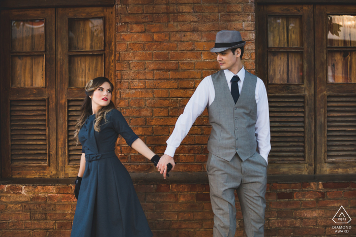 Petrópolis couple e-session in formal attire by a brick building with window shutters Petrópolis couple e-session in formal attire by a brick building with window shutters