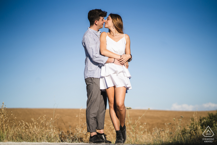 Sesión electrónica para parejas en Siena, Toscana abrazándose y besándose con cielos azules