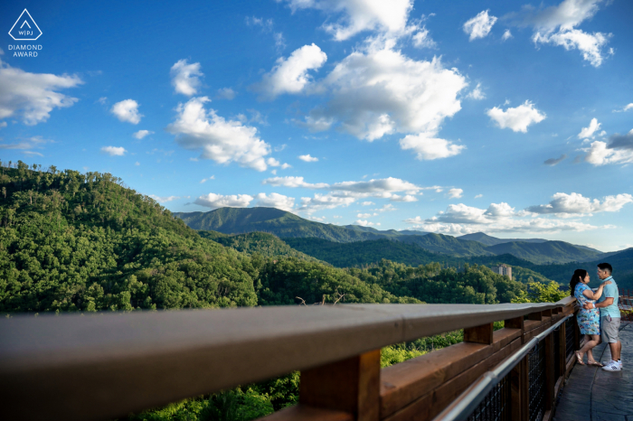 Anakeesta, Gatlinburg coppia e-session in TN abbracciata contro una ringhiera mentre vediamo le grandi montagne fumose sullo sfondo in una bella giornata di sole