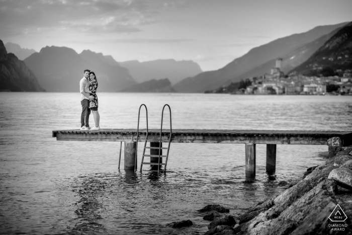 Gardasee-Paar-E-Shooting für ein Verlobungsporträt auf einer Seebrücke mit Blick auf das Städtchen Malcesine und die Berge