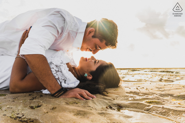 Pareja de Maceió e-shoot tumbados en la arena de la playa con un sol bajo