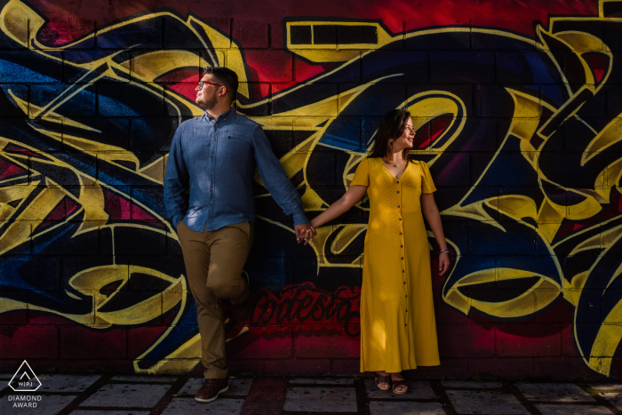 Los futuros novios de San José, CR, posando para una imagen de compromiso en el Paseo Los Damas mientras se toman de la mano posando en un muro de graffiti