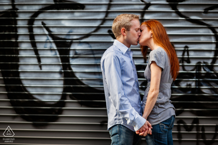 San Francisco bride and groom to be, posing for a pre-wedding engagement photo shoot with A loving kiss before a city art mural