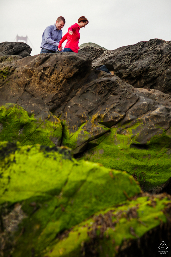 San Francisco bride and groom to be, posing for a pre-wedding engagement photo shoot of the couple having fun navigating through the mossy rocks