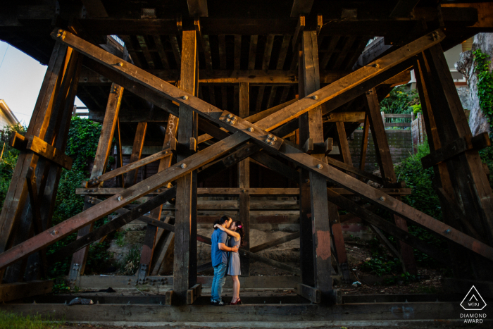 Braut und Bräutigam aus Santa Cruz posieren für ein Verlobungs-Fotoshooting vor der Hochzeit des Paares, das sich unter der hölzernen Eisenbahnbrücke umarmt und küsst