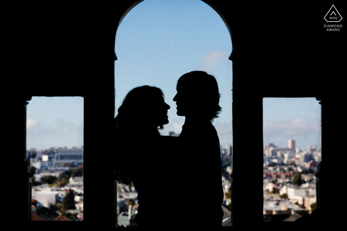 Futuros noivos em São Francisco, posicionando-se para uma imagem de noivado da silhueta dos amantes com a vista da cidade como pano de fundo