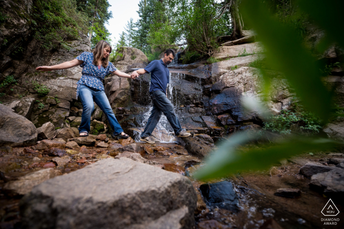 Retratos al aire libre de Maxwell Falls, Colorado, fotografía de compromiso con una pareja navegando rocas por cascada