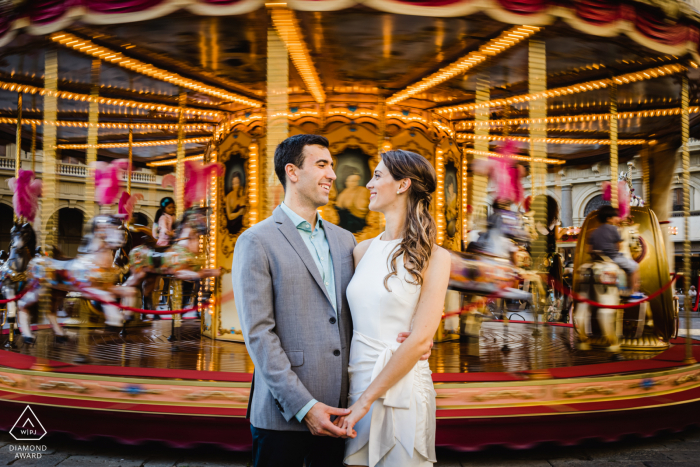 Sessão de imagens pré-casamento de casal ambiental de Firenze em frente a um carrossel desfocado na feira