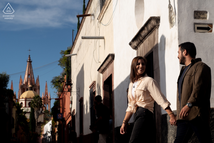 Sessão de imagens de noivado do casal de San Miguel de Allende antes do casamento na Calle Aldama enquanto caminha de mãos dadas na vila sob o sol