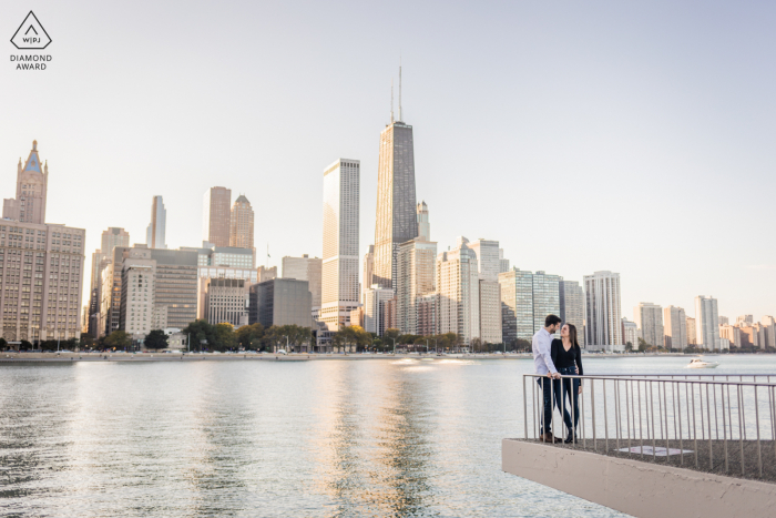 Portrait-Session vor der Hochzeit im Olive Park, Chicago, während sich das Paar mit der Skyline von IL bei Sonnenuntergang hinter ihnen küsst