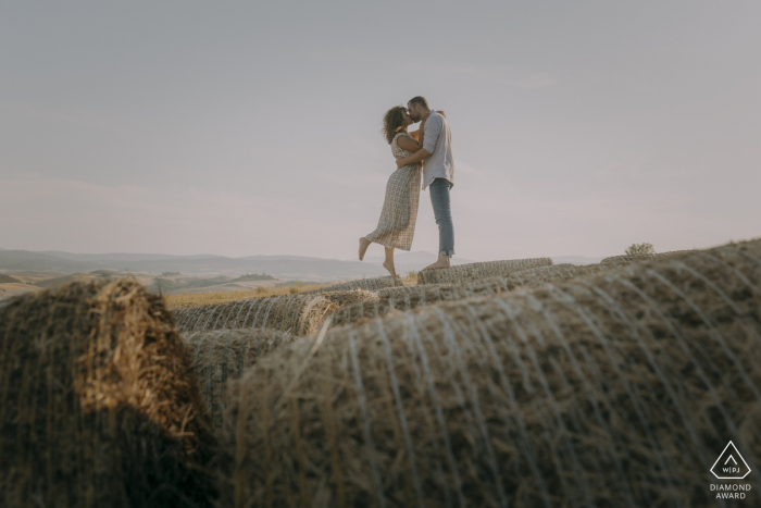 Sessão de retratos antes do casamento em Siena, Toscana, com um pouco de amor na ponta dos pés sobre fardos de feno embrulhados em ambiente rural no interior