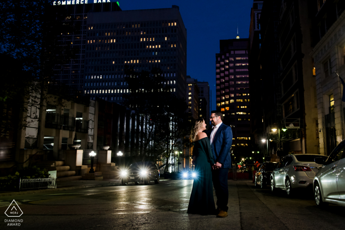 Retratos de noivado de casal no centro de Kansas City com um casal com as luzes do centro à noite na cidade