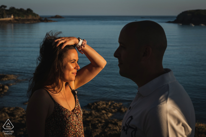 Casal apaixonado e divertido de Saint-Coulomb modelando para uma sessão pré-casamento sob o sol baixo perto da água