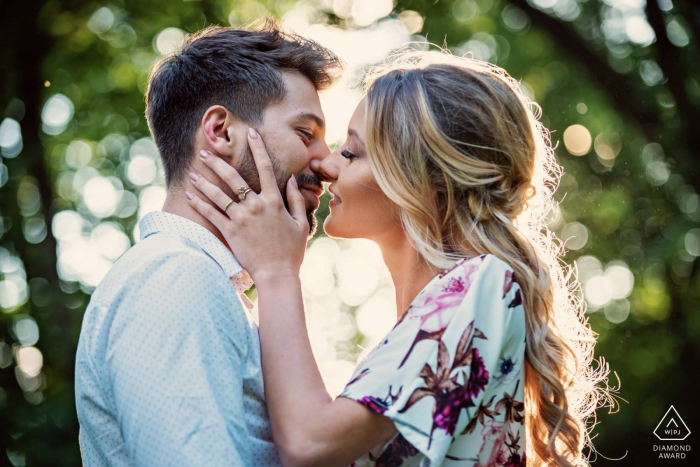 Una romántica y dulce foto de compromiso de Mlochow para una pareja celebrando el día de su compromiso, un momento de tiernos besos, mientras el sol dorado ilumina bellamente sus siluetas