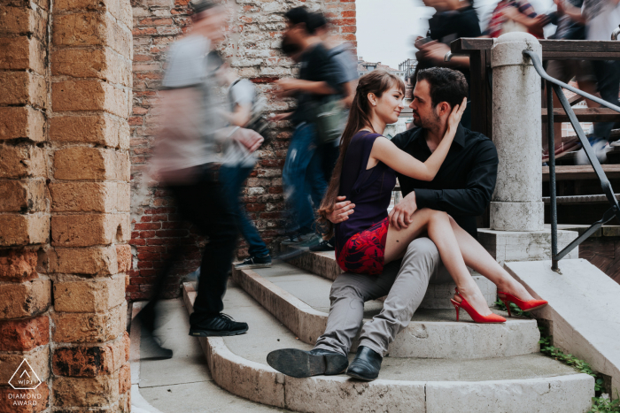 Uma sessão romântica de pré-casamento em Veneza com um casal italiano sentado em degraus com pedestres passando em desfoque de movimento da velocidade lenta do obturador