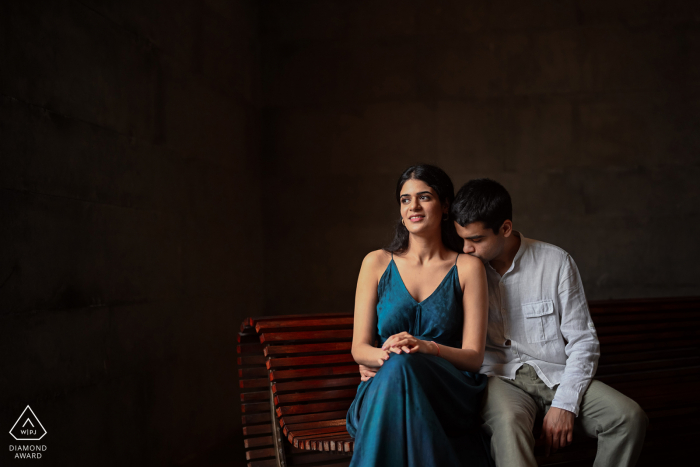 An India Wedding, Elopement, and Engagement Photographer created this artistic, romantic portrait of this Chennai couple sitting on a bench as the groom to be kissing the shoulder of his future bride