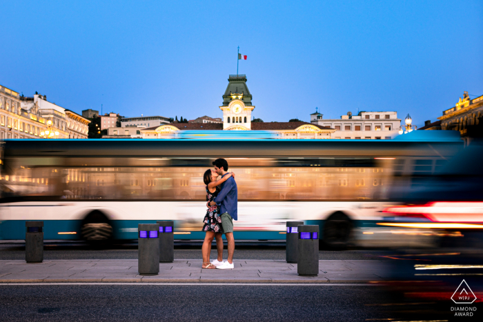 Ein Hochzeits-, Elopement- und Verlobungsfotograf aus Udine hat dieses künstlerische, urbane Porträt dieses Paares aus Triest vor einem langsam fahrenden Bus erstellt