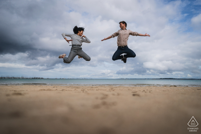 A France Wedding, Elopement, and Engagement Photographer created this creative, beach portrait of this Saint Cast couple jumping with a sense of humor on a beach