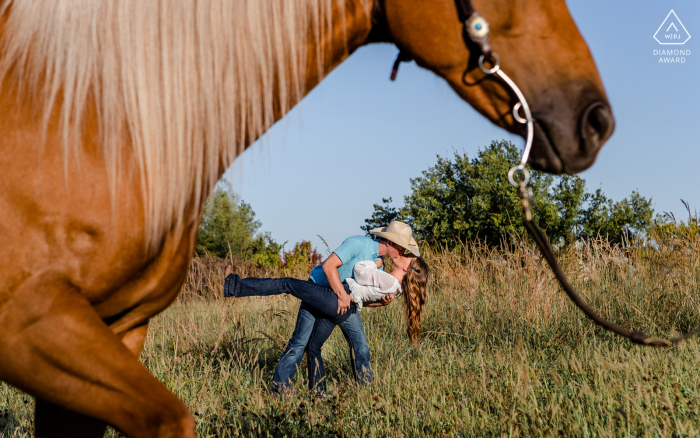 Nebraska lifestyle portraits session with a horse in the foreground, and the couple kissing and dipping in background 