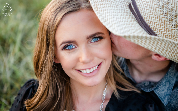 A Nebraska lifestyle couple photo session showing a girl kissed by her boyfriend in a cowboy hat 