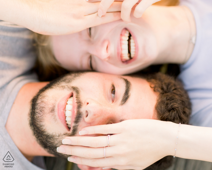 Paris lifestyle portrait photography in Ile de France for a Couple laughing while lying on their backs, shot from above 