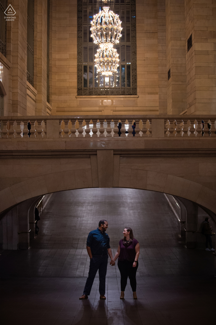 Grand Central Station post fotos de retratos de proposta de um casal feliz de Nova York de mãos dadas sob um arco e candelabros na estação de trem