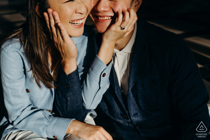 Singapore post proposal photography showing a smiling Asian couple touching each others faces in the sunshine Singapore post proposal photography showing a smiling Asian couple touching each others faces in the sunshine