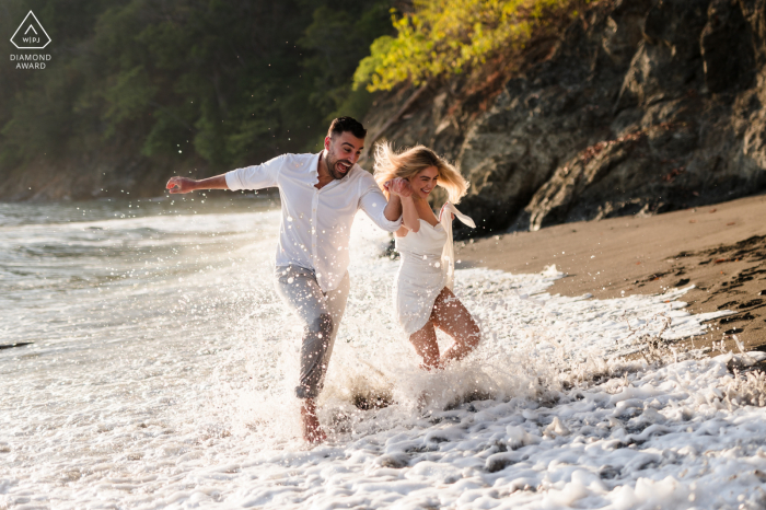 Marina Los Sueños publica fotos de retrato de propuesta de una feliz pareja costarricense corriendo por el agua durante su sesión de compromiso en la playa