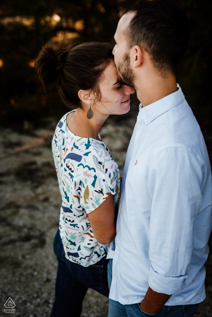 Occitanie publica retratos de propuestas realizados por un fotógrafo de bodas de Montpellier de una feliz pareja francesa de pie mientras él la besa en la frente