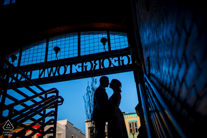 Georgetown-Post-Proposal-Porträtfotos eines glücklichen Paares aus Washington DC, das dicht beieinander steht, mit dem Georgetown-Schild, das ebenfalls im Hintergrund zu sehen ist