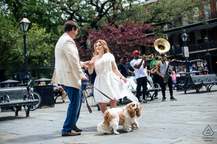 Una soleada Sesión de Compromiso del Distrito de las Artes de Nueva Orleans en el Barrio Francés de Orleans de la pareja bailando en la calle con una banda de música en vivo con sus 2 perros