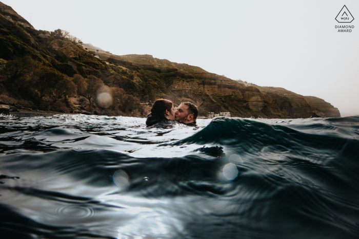 Adventurous engagement photos in Santorini with the couple wading into the water