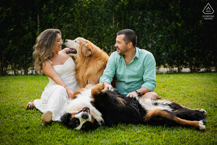 Photos de fiançailles de Petropolis. Couple de Rio de Janeiro posant avec des chiens sur l'herbe verte et luxuriante de la scène du parc