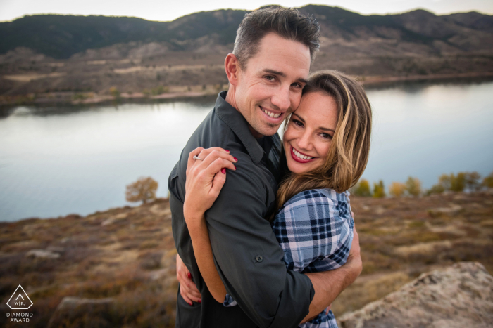 Engagement Photos Horsetooth Reservoir. A Fort Collins Couple hugging and looking at camera overlooking reservoir