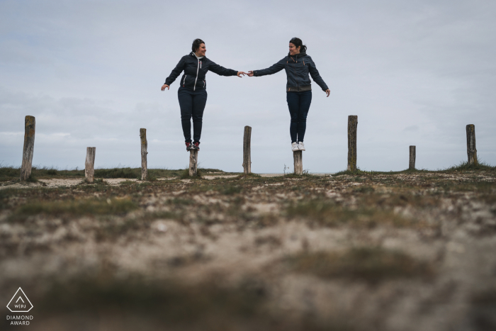 Sessão de fotos de noivado de Hirel em Ille-et-Vilaine, Bretanha, para um casal francês de mãos dadas e se equilibrando em postes de madeira