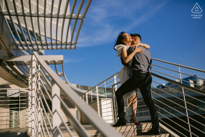 Un Save the Date à San José. Portrait californien d'amants embrassés en haut des escaliers sous un ciel bleu