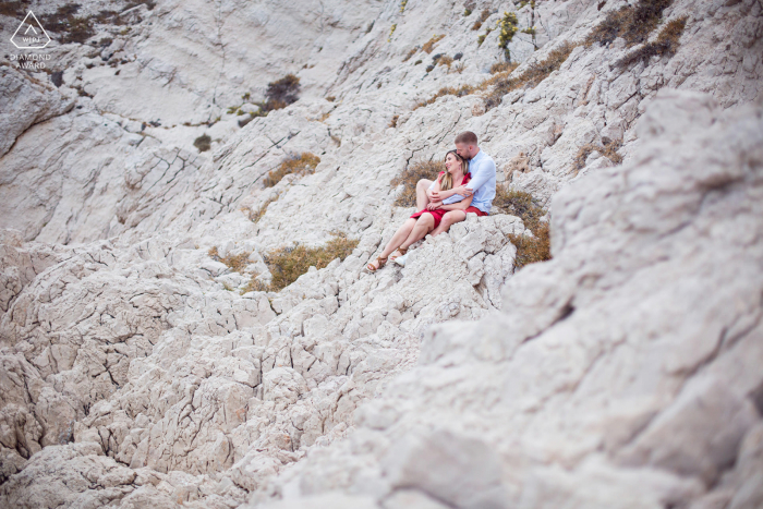 A Montreal couple poses for a beach portrait together as they prepare to announce their Les Goudes engagement while hugging on a cliff above the sea