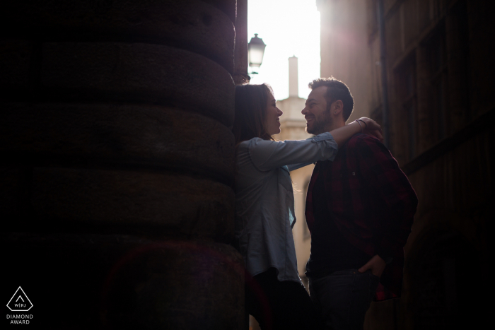 Un couple lyonnais pose pour des portraits en intérieur pour annoncer ses fiançailles françaises avec The sun piercing through building et illuminant leurs sourires