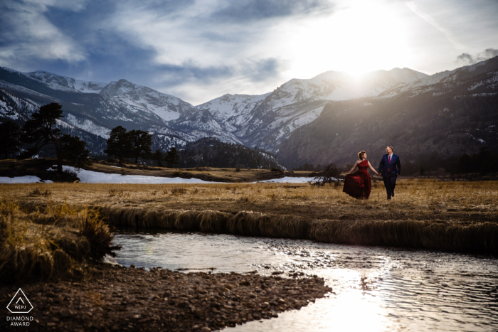 Una coppia del Colorado cammina insieme tenendosi per mano vicino all'acqua mentre si preparano ad annunciare il loro fidanzamento RMNP