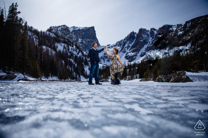 A newly engaged Colorado couple poses on the ice and snow for a Rocky Mountain National Park engagement announcement portrait A newly engaged Colorado couple poses on the ice and snow for a Rocky Mountain National Park engagement announcement portrait