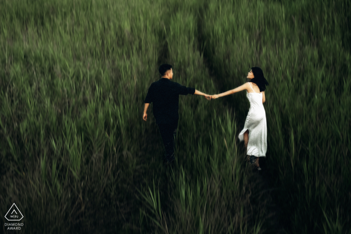 A newly engaged Xian couple is running in the grass outdoors for a China engagement announcement portrait