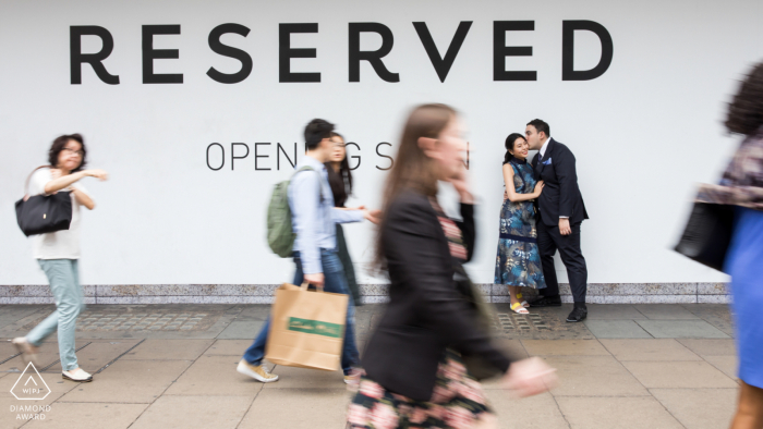 A London couple posing on Oxford Street for an engagement announcement portrait on a major road in the City of Westminster in the West End of London between Tottenham Court Road and Marble Arch via Oxford Circus