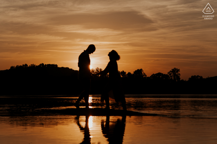 Ein modernes Sancerre-Paar posiert für ein Wasserreflexions-Ankündigungsporträt während des Sonnenuntergangs ihrer Verlobung im Centre-Val de Loire