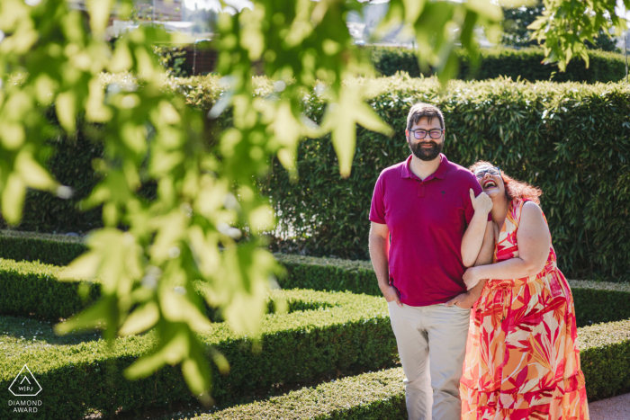 Um casal Mondorf Laughing recém-noivo com folhas em primeiro plano posando para um retrato de anúncio de noivado de Luxemburgo