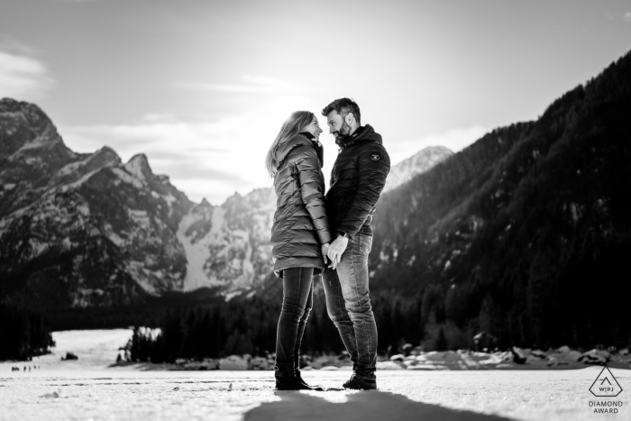 Una pareja de Udine se aventura junta sobre el lago helado para una sesión de retratos en blanco y negro del anuncio de compromiso moderno del lago Fusine Tarvisio