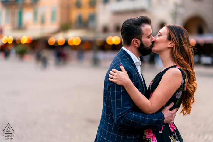 Um casal moderno de Verona posa para um retrato de anúncio mais casual e pessoal de seu noivado na Itália com um beijo doce nas ruas urbanas perto do anoitecer