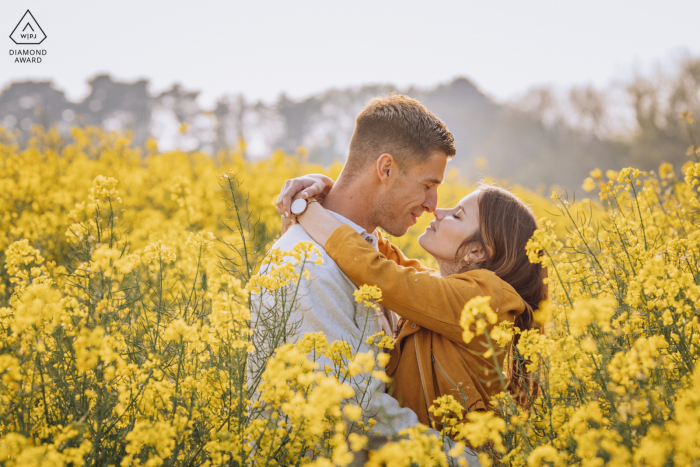 Casal de noivos de Ouistreham ultra-bonito posando durante uma sessão de fotos para anunciar seu noivado em Calvados, Normandia, França, criado quando eles estão prestes a se beijar em um campo de colza