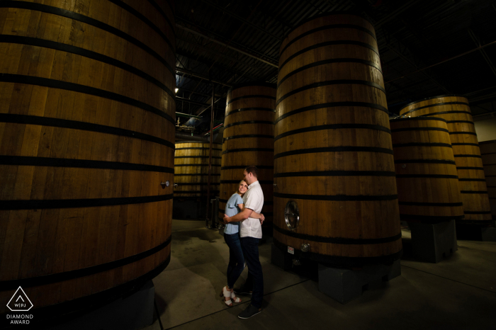 Idée de photo d'annonce de fiançailles de Fort Collins à la New Belgium Brewery créée alors que le couple profite d'une minute ensemble parmi les grands fûts de bière aigre dans une brasserie locale