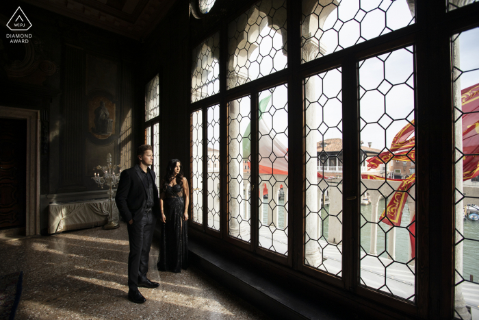 Tournage de fiançailles à destination de Venise pour un couple italien à l'hôtel Ca 'Sagredo alors qu'ils regardent depuis une vieille fenêtre à l'intérieur d'un palais historique en Italie